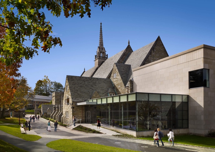 Modern stone and glass addition to the back of Goodhart Hall with students walking by.