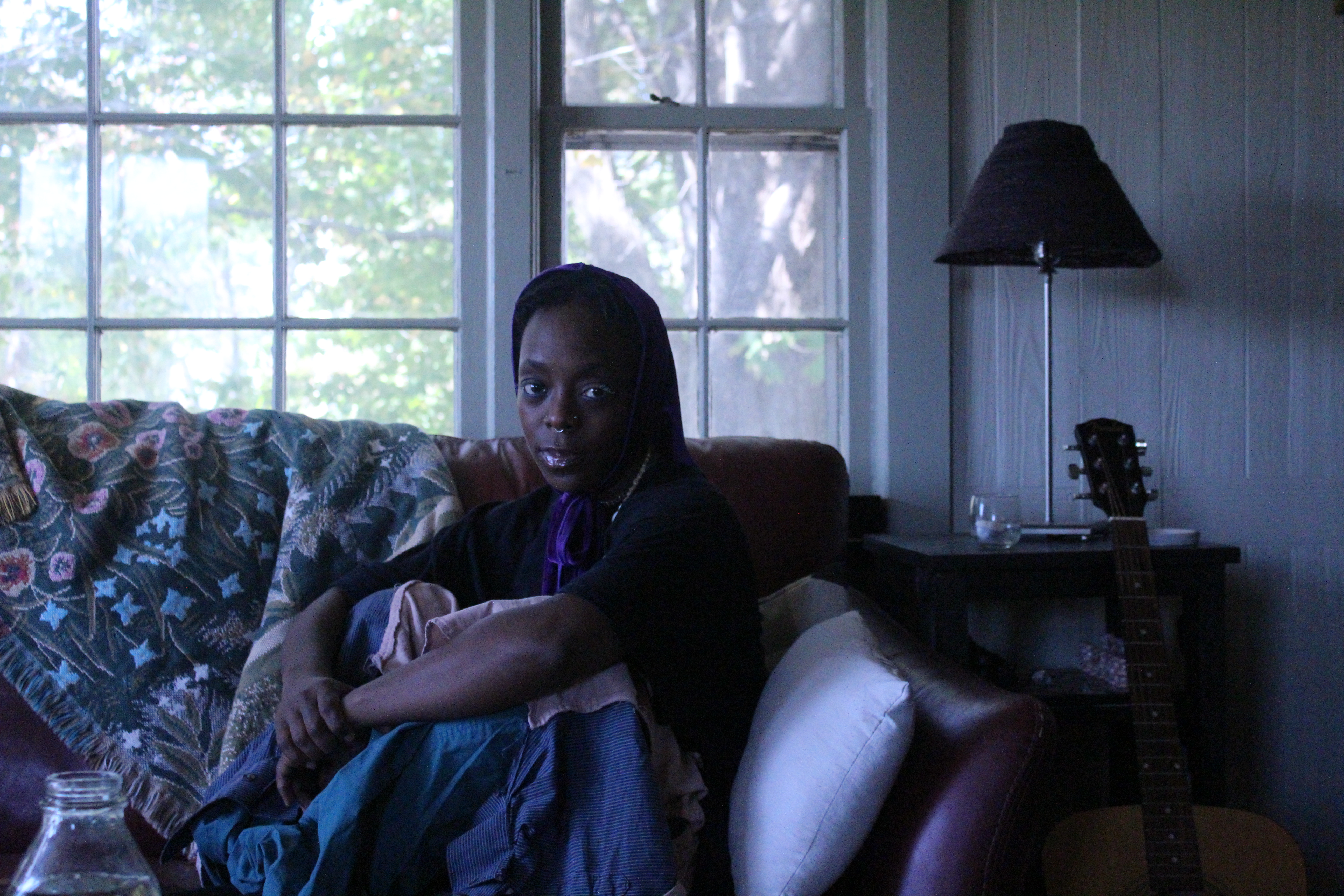 A brown skin person sitting on a couch in front of a window. 