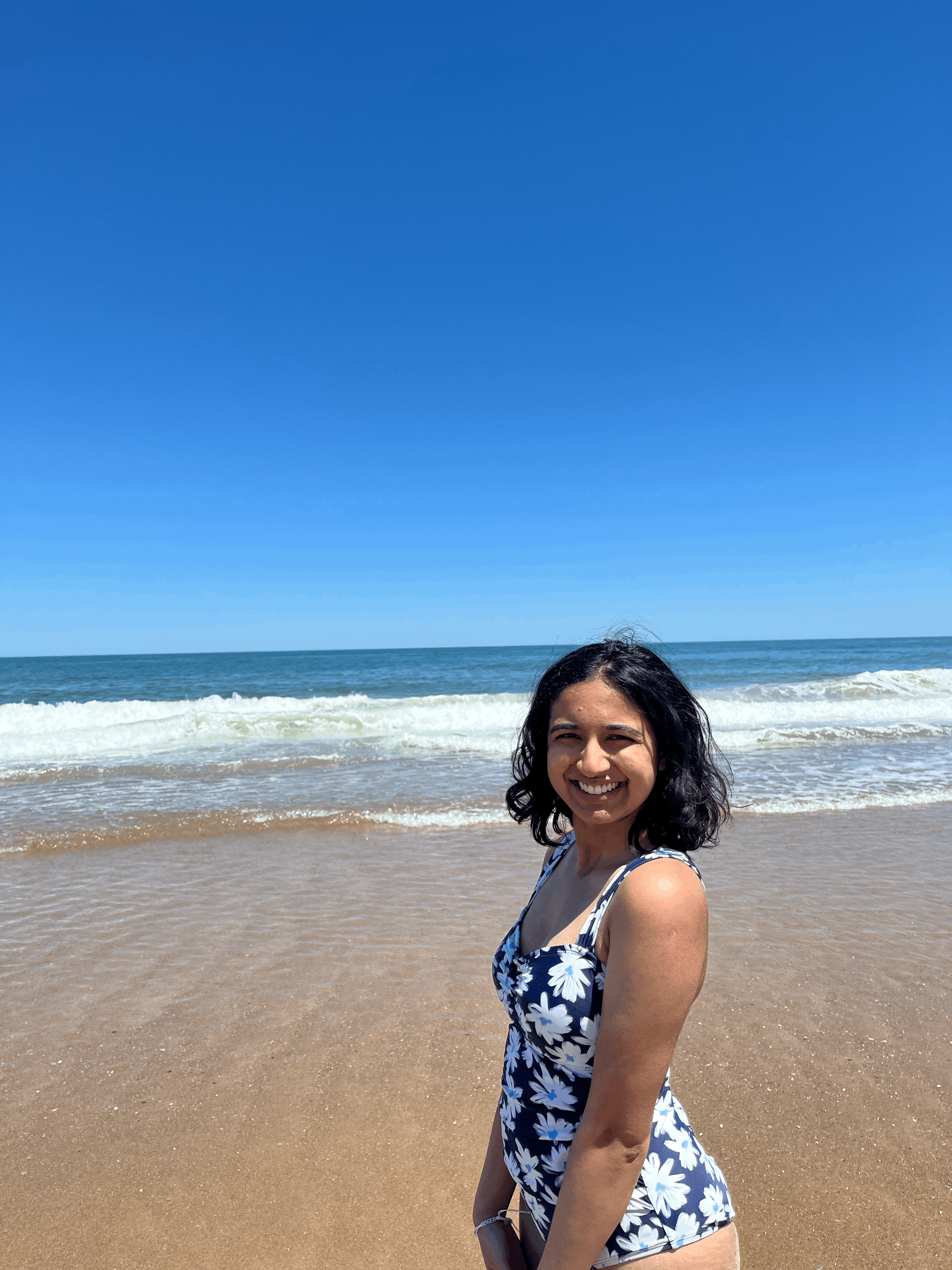 Ambar in a swimsuit standing in front of waves at a beach.